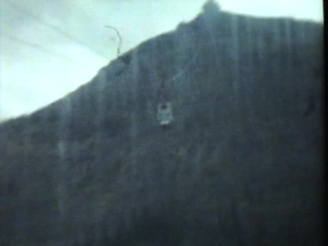 A young family takes a gondola cable car ride up the side of a mountain to view the beautiful surroundings while on their summer vacation.