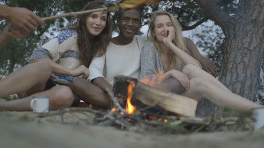 Young man smoking fish on campfire with friends