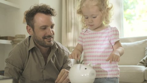 Father helping daughter to save money in piggy bank