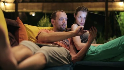 Couple watching something on tablet computer on sofa at home
