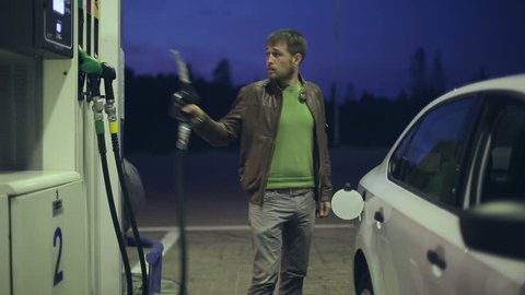 Filling station. A man fills his car with gasoline at night