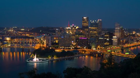 (Time-lapse/Zoom-in) Night falls on the downtown area of Pittsburgh, Pennsylvania including the skyline, bridges, and Point State Park at the confluence of the Allegheny and Monongahela Rivers.
