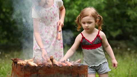 Two little girl makes barbecue on the grill at green lawn.
