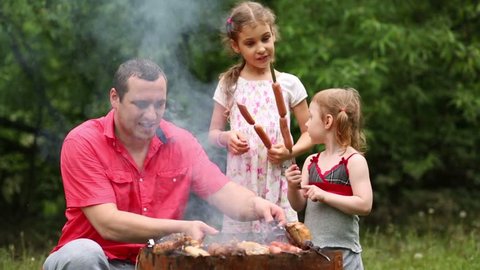 Family of three makes barbecue on the grill at green lawn.