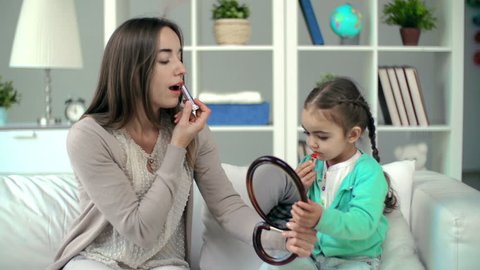 Mother showing daughter lipstick applying technique, girl failing to rouge correctly but having lots of fun