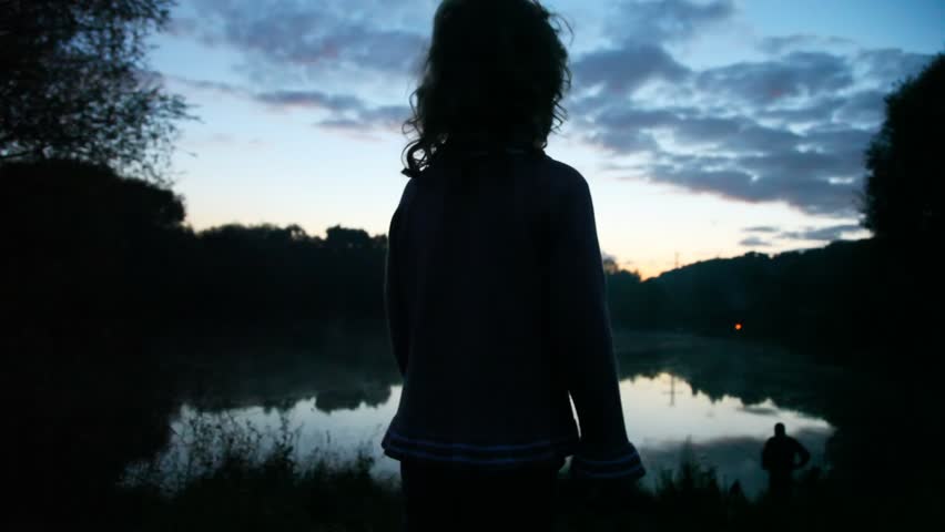 little girl lifts hands standing at lake in wood at dawn 