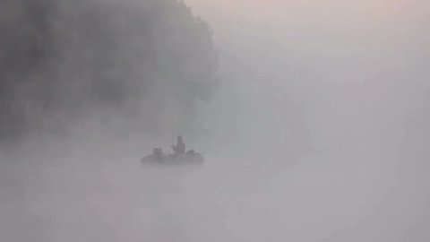 The fisherman in the boat on the strong foggy water surface. Early morning. Very original shot. Footage taken with Red Cinema Camera