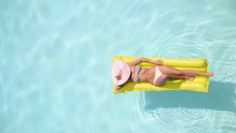 Beautiful young woman relaxing on a yellow inflatable mattress in a swimming pool - Pretty model with perfect shapes chilling out in a exotic resort