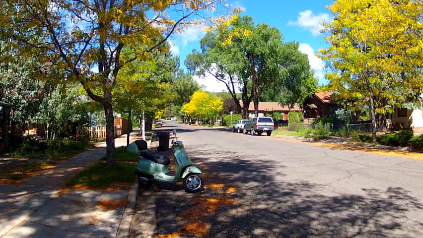 FLAGSTAFF, AZ: September 20, 2014- A blue scooter is parked at a curb in a small neighborhood circa 2014 in Flagstaff. Fuel efficient vehicle is parked under a shade tree along a residential street.