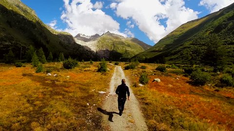 young man running on nature road into mountain landscape panorama. aerial fly over