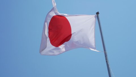State Japanese flag on the strong wind over blue sky background