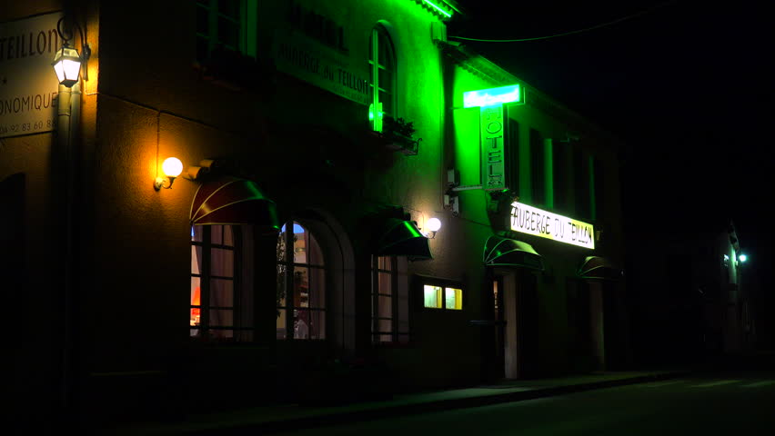 A small French hotel at night with neon sign flashing.