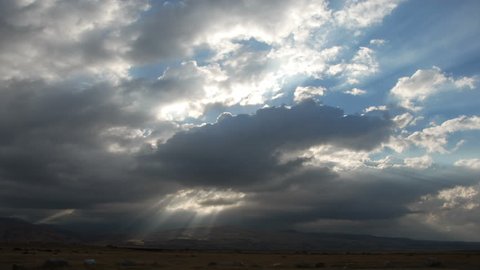 Time lapse storm clouds with light rays billow over plains and mountains.