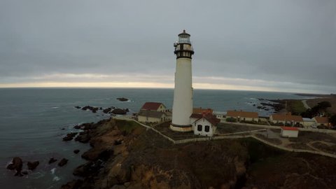 AERIAL: Tracking HD 4K establishing shot of lighthouse on a moody overcast day near a Pacific coastline during sunset  Arkivvideo