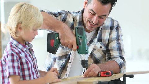 Man with little boy using electric drill
