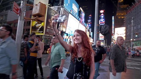 NEW YORK - AUGUST 9, 2014: tourist takes selfie with smartphone in Times Square at night in 4K in New York. Times Square is a major intersection and neighborhood in Manhattan, NYC.