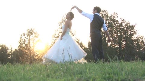 Model released bride and groom dancing together in grassy field during sunset on their wedding day.