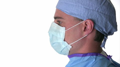 Surgeon rotates to face the camera and takes off his mask then smiles.