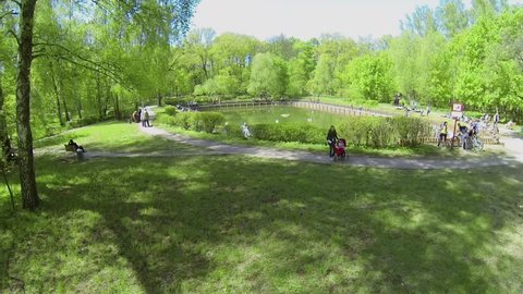 People walk around Sobachii pond in park at spring sunny day. Aerial view