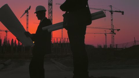 Steadicam shot of skyline and cranes with Asian construction/ executive/ architect/ engineer consultant discussing blue print of new urban development with caucasian construction executive at sunset. Stock Video