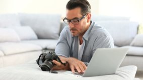Man at home using digital camera and laptop 