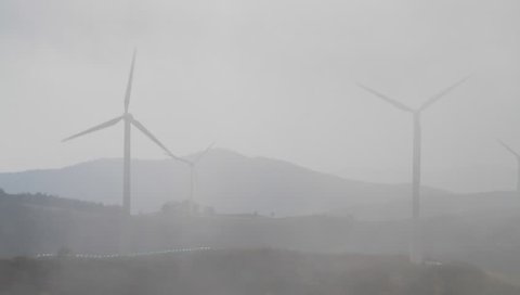 Wind farm with wind turbines making green energy covered with foggy clouds