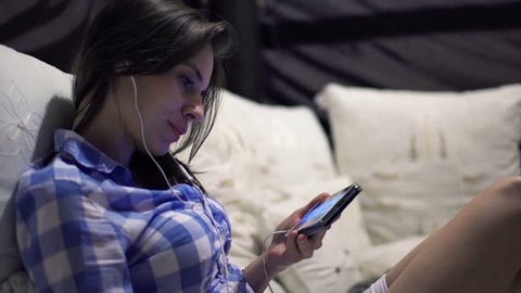 Young woman watching movie on smartphone on bed at night
