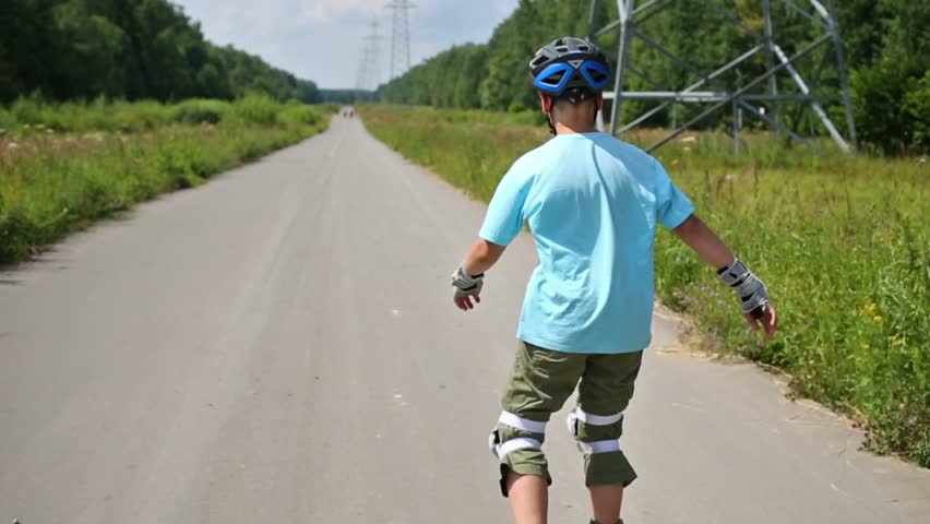 Teenage boy in helmet roller-skates on road in summer day