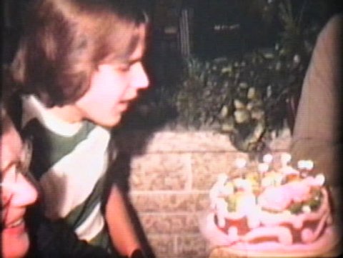 A teenage boy blows out the candles on his unusually pink birthday cake.