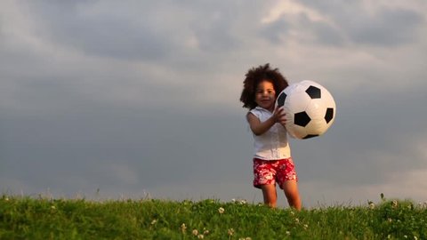 Little cute girl throws inflatable soccer balloon green meadow