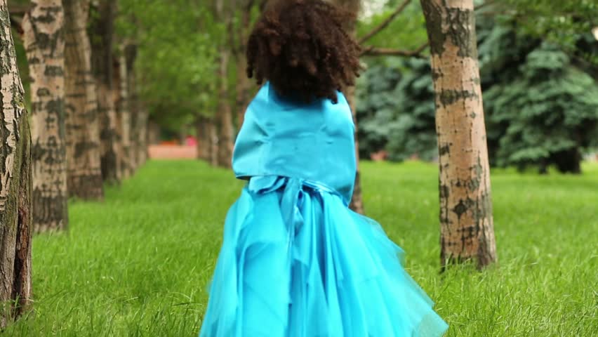 Little girl in blue dress walks between trees in park