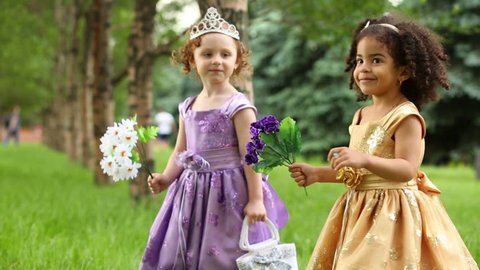 Two little girls in beautiful dresses hold flowers in park
