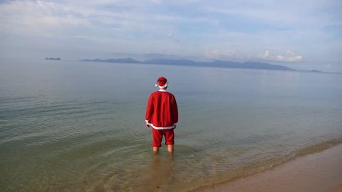 Happy joyful and cheerful Santa Claus on summer holiday, raising arms to the sky in the sea water at tropical beach. Slow motion. HD, 1920x1080.