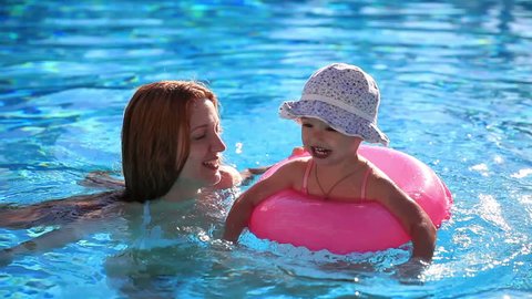 Mother and young daughter swimming in the pool with pink lifeline.