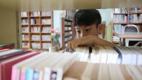 Little Asian student reading book in library . 