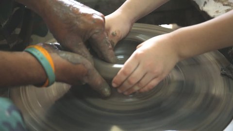 Close up of hands working clay on potter's wheel and little hand learning . 