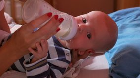 Mother is feeding her adorable baby boy with a bottle. HD stock video.