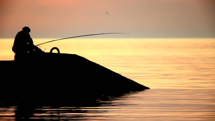 Silhouette of Fisherman at sunset. In the fisherman jerks rod