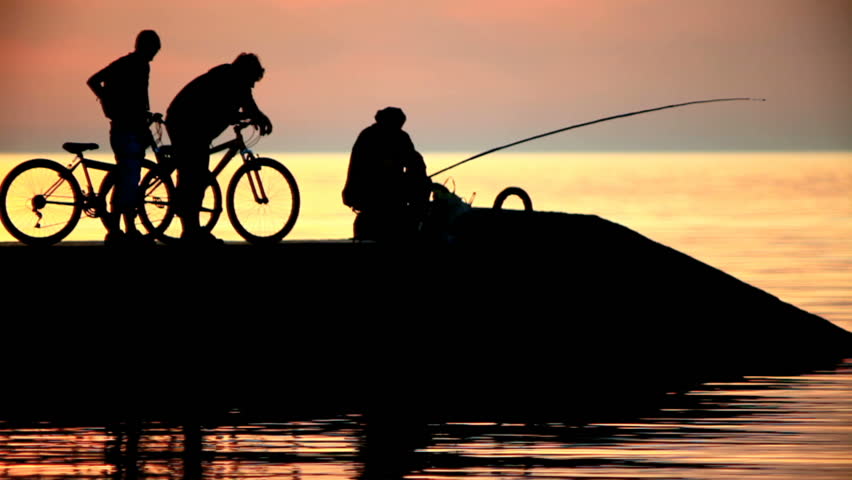 Silhouettes of the fisherman and two cyclists at sunset in the sea