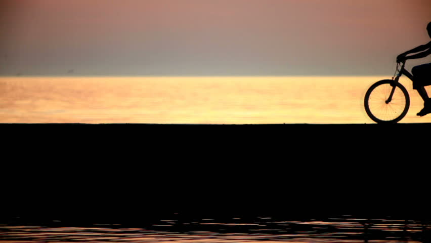 Silhouettes of two cyclists at sunset in the sea. They stopped and talking
