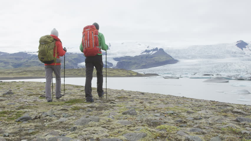 Travel people hiking adventure in Iceland nature. Hikers walking by glacier and glacial lagoon / lake Fjallsarlon, Vatna glacier. Tourist couple in Icelandic Vatnajokull National Park. RED EPIC 60 FPS