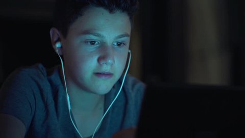 Young teenager watching movie on tablet computer at night
