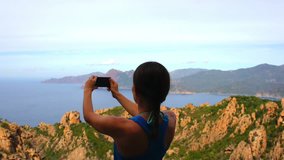 Young woman uses a smartphone to video a beautiful view in the sea, Corsica, Les calanches