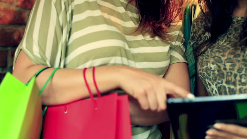 Happy women using tablet in the boutique and holding shopping bags
