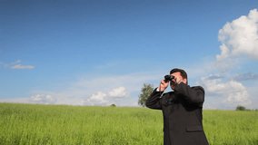 Business man in a field look into binoculars