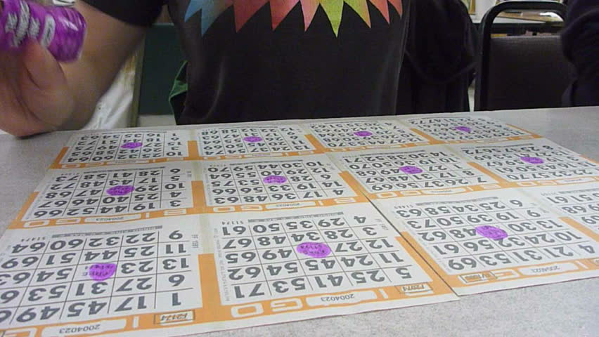 Woman wearing action shirt daubs ink on bingo cards in veteran bingo hall time