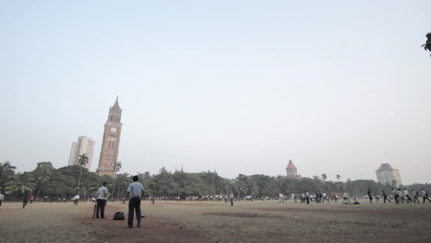 Panning shot of cricket pitches in Oval Maidan, a recreational park in central Mumbai India with the colonial Rajabai clock Tower in background