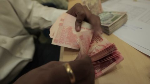 Indian man with golden ring quickly counts a large wad of 20 rupee indian currency bank notes in an office