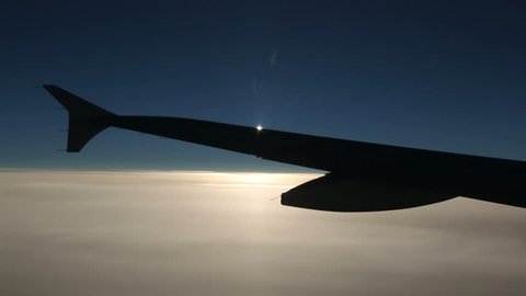 Shadow side of an airplane wing flying over clouds, sun rays appearing behind