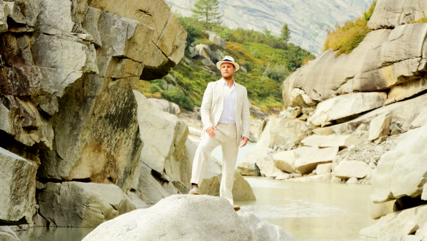 man standing on stone rock raising arms. casual suit clothes. recreational lifestyle background 